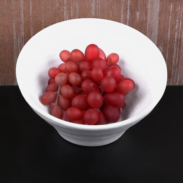 A white Elite Global Solutions Durango melamine bowl filled with red grapes on a black surface.