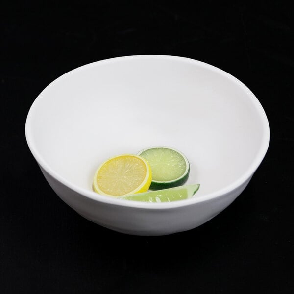 An off white Elite Global Solutions melamine serving bowl with a bowl of fruit including lemon and lime slices.