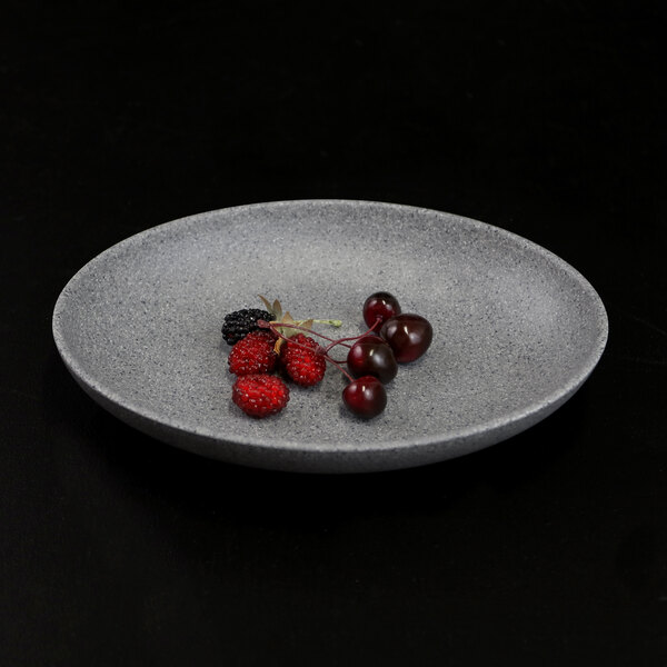 A Tenaya granite stone oval melamine plate with a plate of fruit on it on a black surface.