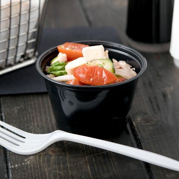 A black Dart plastic souffle cup filled with salad with tomatoes and vegetables.