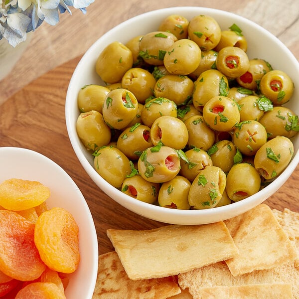 A bowl of green olives next to a plate of crackers.