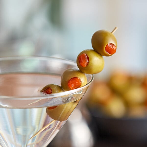 A close up of a martini with Queen olives on a skewer.