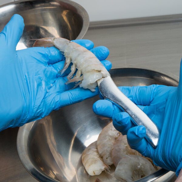 A person in blue gloves using a Winco shrimp deveiner to cut a shrimp.