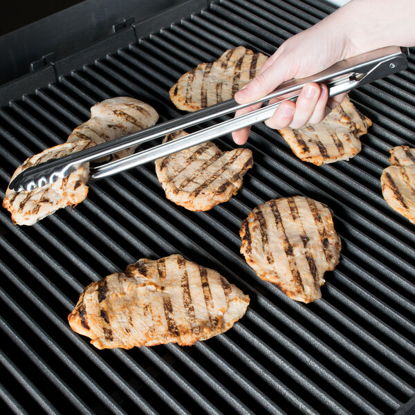 A person using Edlund heavy-duty scallop tongs to pick up a piece of meat on a grill.