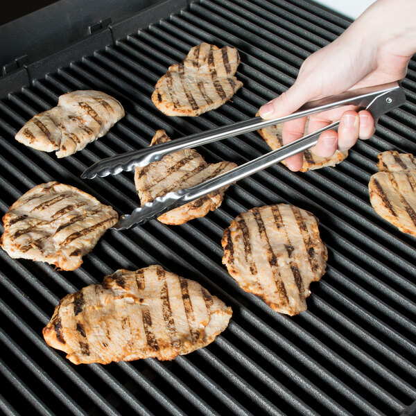 A person using Edlund heavy-duty scallop tongs to grill meat.