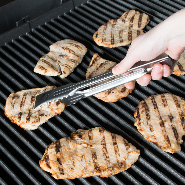 A person using Edlund heavy-duty tongs to grill chicken