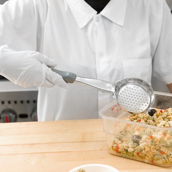 A person in a white shirt and gloves using a Vollrath gray perforated round Spoodle to serve pasta from a plastic cup.