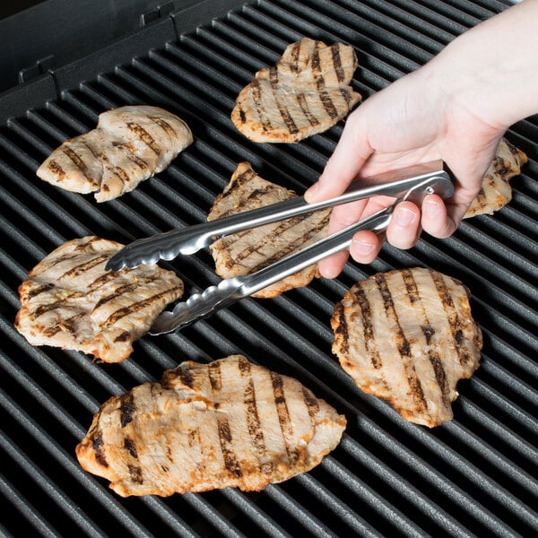 A person using Edlund heavy-duty scallop utility tongs to grill meat.