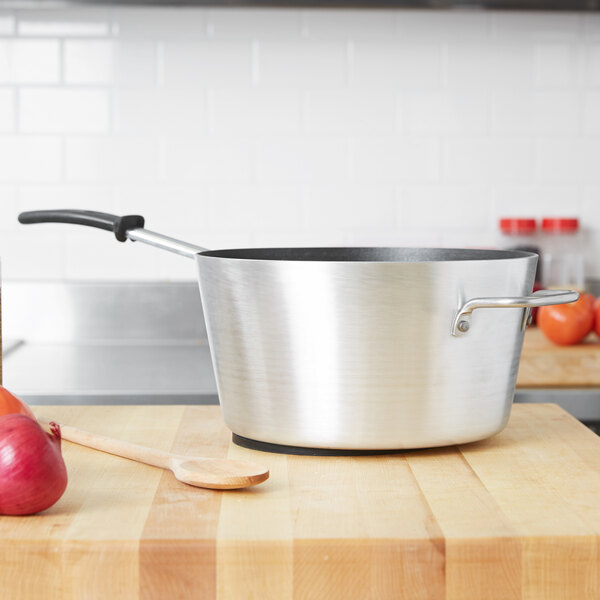 A Vollrath Wear-Ever sauce pan with a wooden spoon on a wooden surface.