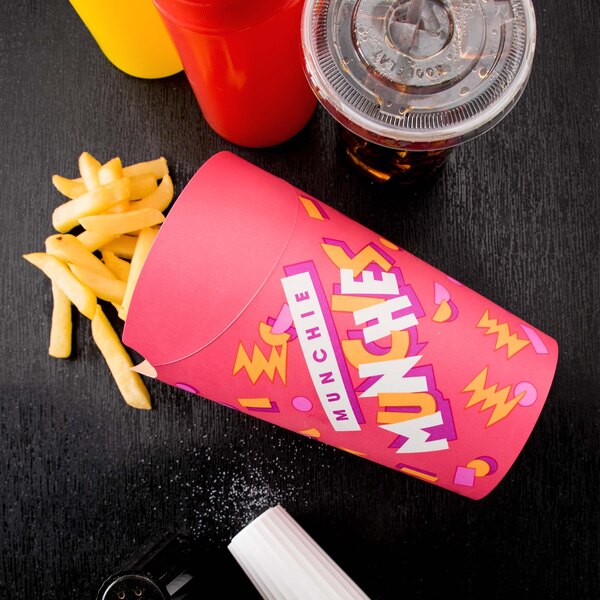 A pink Solo paper container of french fries and a drink on a table with a red bottle and a plastic cup with a lid.
