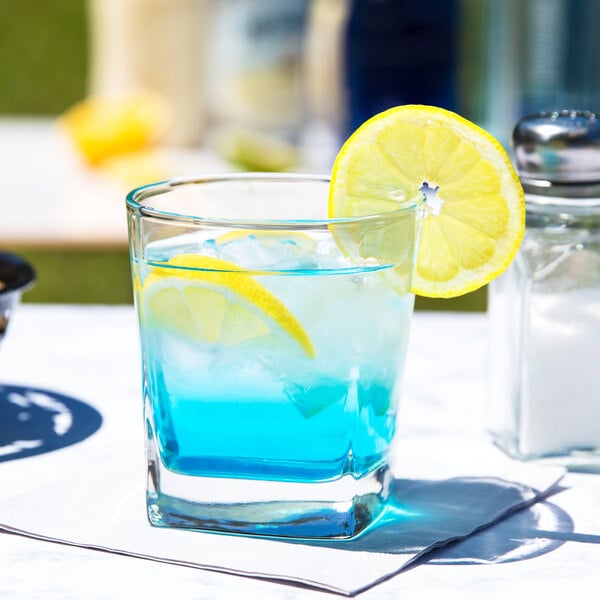A Libbey old fashioned glass with blue liquid and a lemon slice on the rim.