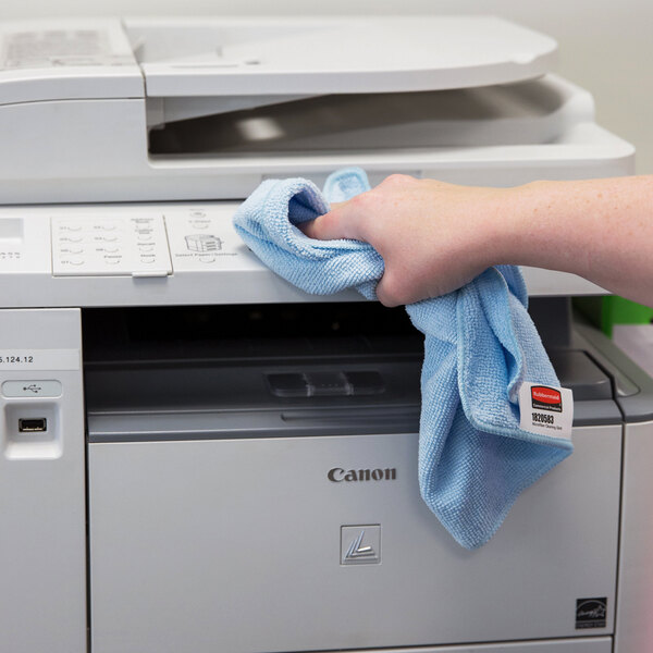 A hand using a blue Rubbermaid Microfiber Cloth to clean a printer.