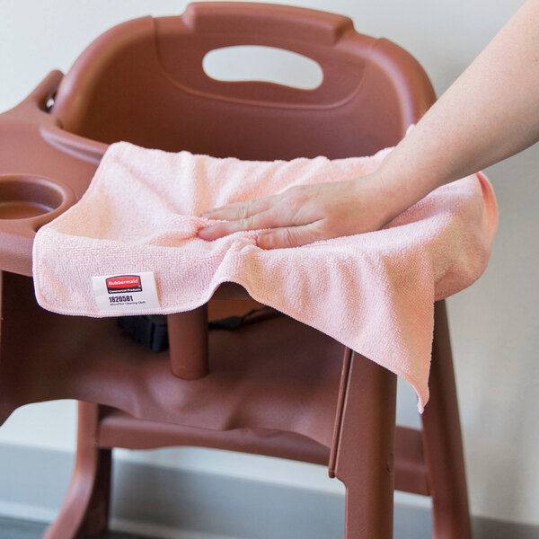 A hand using a pink Rubbermaid microfiber cloth to wipe down a high chair