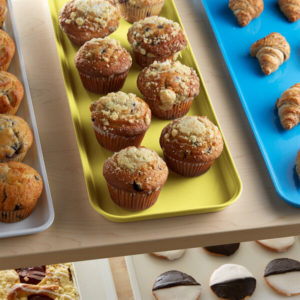 A yellow Cambro fiberglass market tray holding muffins on a table in a bakery display.