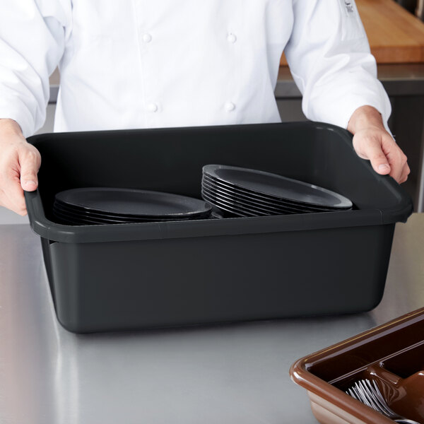 A chef holding a black Cambro bus tub with plates in it.