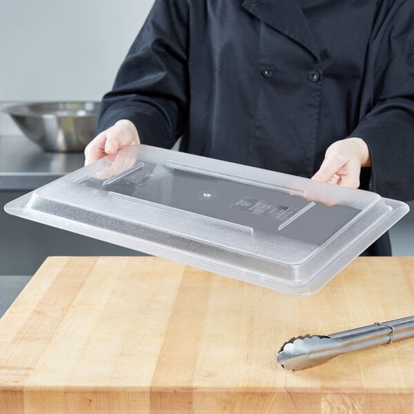 A chef using a Carlisle clear plastic lid to cover a food storage container on a counter.