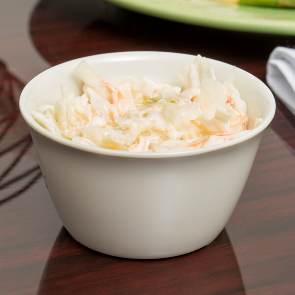A Carlisle bone melamine bouillon cup filled with coleslaw on a table.