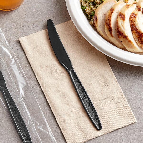 A close up of a black Visions plastic knife on a table next to a plate of food.