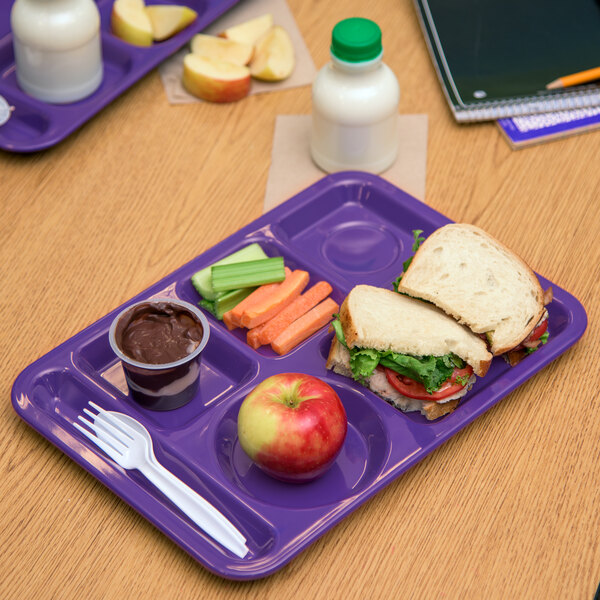 A Carlisle purple 6 compartment tray with a sandwich, apple, and carrot on it.