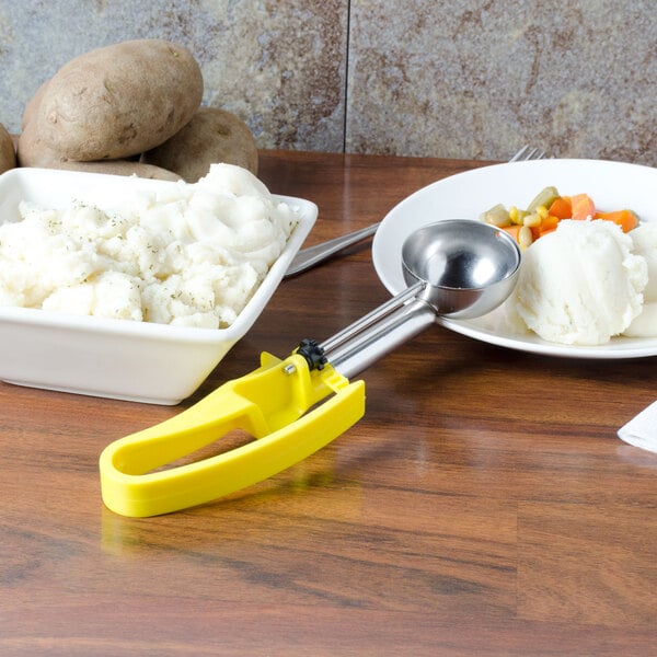A yellow Vollrath extended length disher next to a bowl of mashed potatoes.