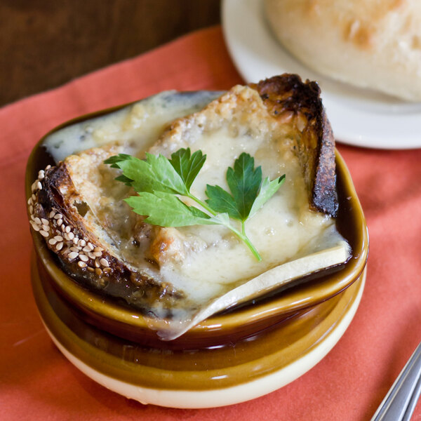 A Tuxton two tone onion soup crock filled with soup and topped with cheese and parsley.