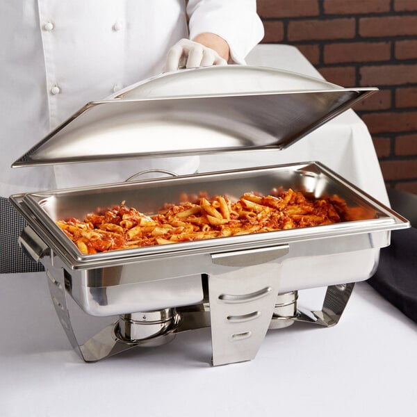 A person using a Vollrath Maximillian steel rectangular chafer to serve pasta on a table outdoors.