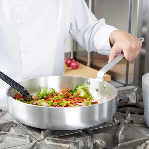 A chef cooking vegetables in a Vollrath Wear-Ever saute pan.