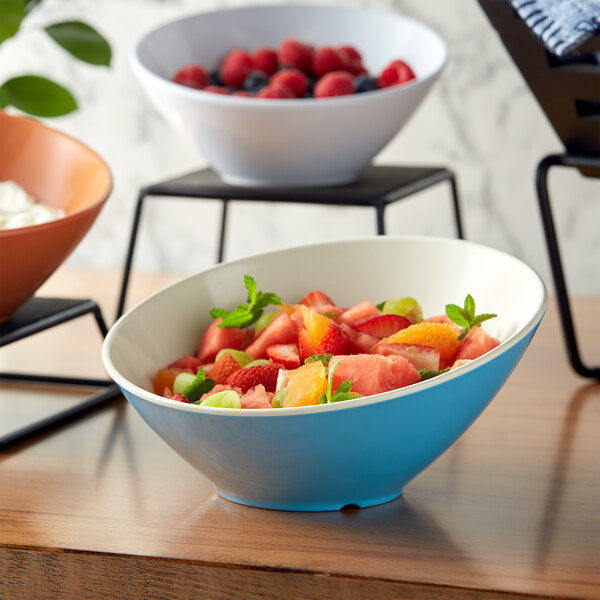 A white slanted melamine bowl filled with fruit and berries.