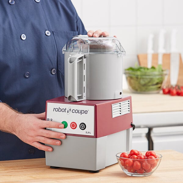 A man using a Robot Coupe food processor to chop cherry tomatoes.