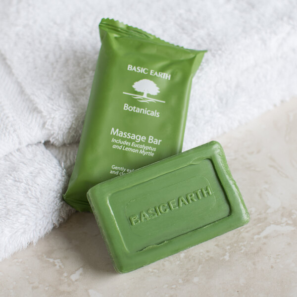 A green Basic Earth Botanicals wrapped massage bar of soap next to a towel.