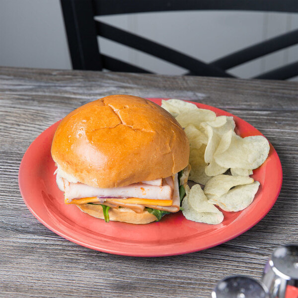 A GET Rio Orange melamine plate with a sandwich and chips on it.