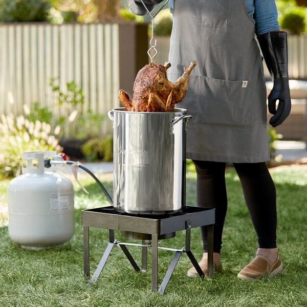A woman using a Backyard Pro stainless steel pot to cook chicken on a grill.
