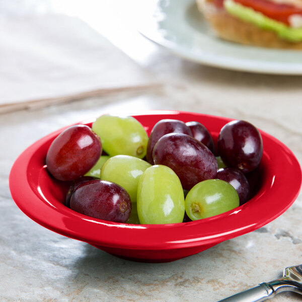 A red Carlisle melamine fruit bowl filled with green, red, and yellow grapes.