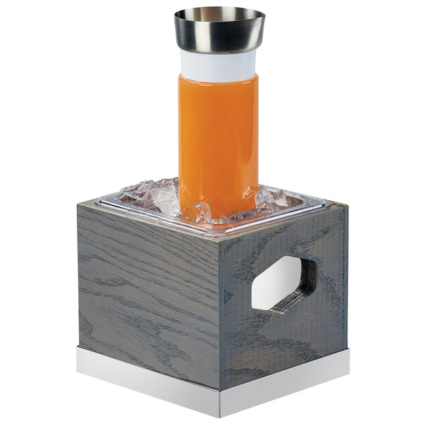A Cal-Mil gray oak wood ice housing container with ice and an orange juice container on top.