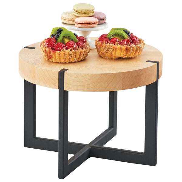 A round maple display riser on a table with fruit on it.