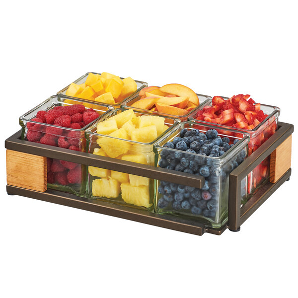 A Cal-Mil Sierra bronze metal and rustic pine organizer with square glass jars filled with different fruits on a table.