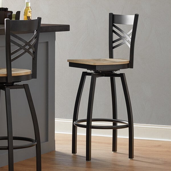 Two Lancaster Table & Seating black swivel bar stools with driftwood seats at a bar counter.
