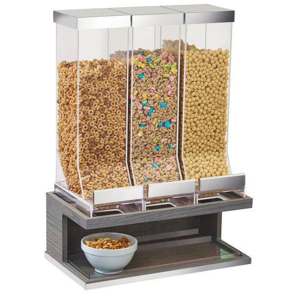 A Cal-Mil Ashwood cereal dispenser with three canisters holding cereal above a bowl.