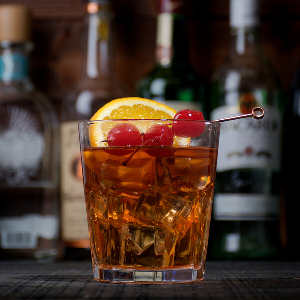 A close-up of an Arcoroc Gotham Double Old Fashioned Glass with alcohol, cherries, and an orange slice.