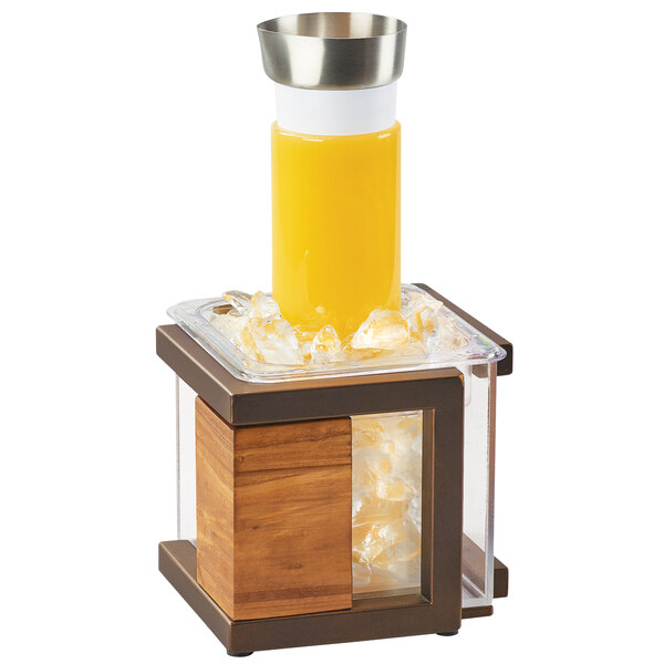 A Cal-Mil Sierra Bronze metal and rustic pine ice housing on a table with a glass of orange juice in it.