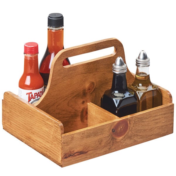 A wooden Cal-Mil condiment caddy with 4 sections holding bottles of sauce and liquid on a table.