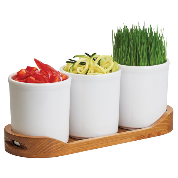 A wooden tray with three white cylinder jars filled with vegetables.