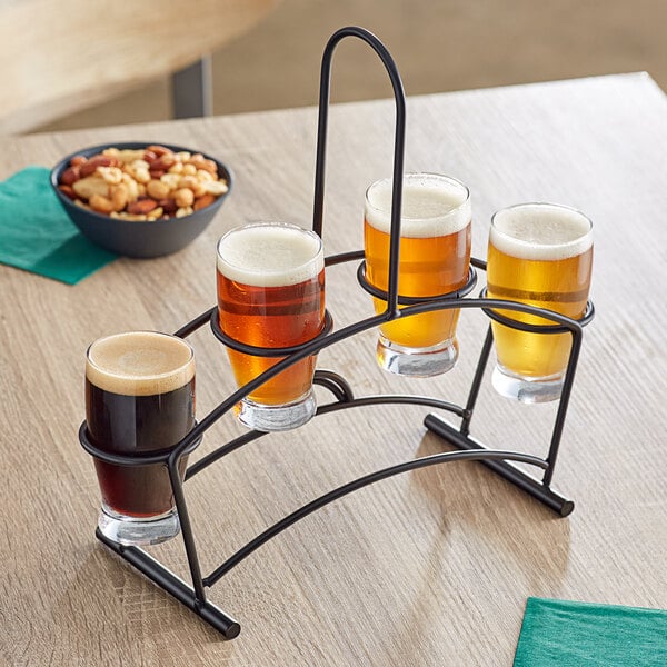 An Acopa metal flight carrier holding four Barbary tasting glasses of beer on a table in a brewery.