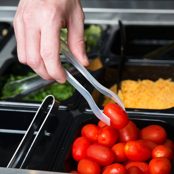 A hand uses Sabert clear plastic tongs to serve tomatoes at a salad bar.