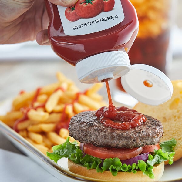 A hand squeezing Red Gold ketchup onto a hamburger.
