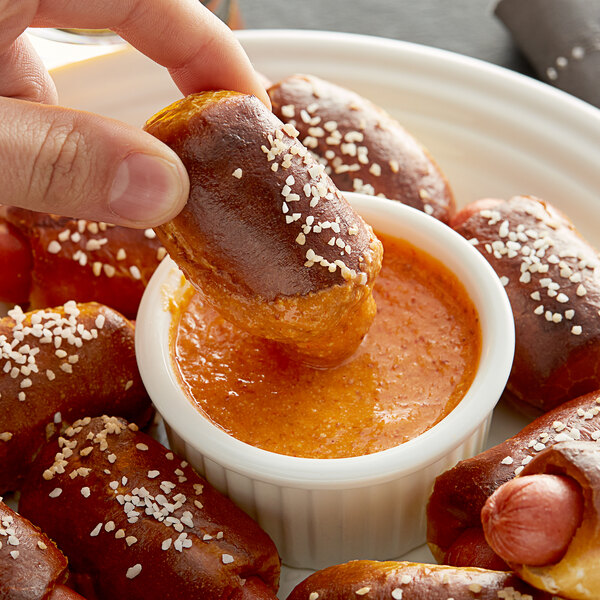 A person dipping a pretzel into Pilsudski Sriracha Mustard.