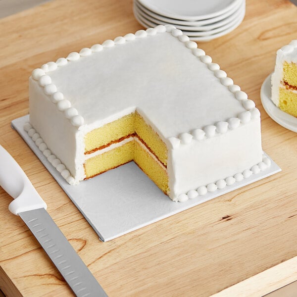 A white square cake on a white Enjay cake board with a slice cut out.
