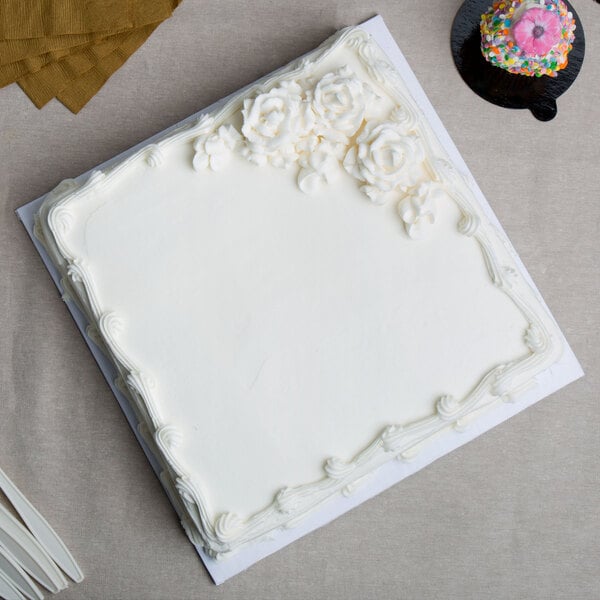 A white square cake with frosting on a white Enjay cake drum.