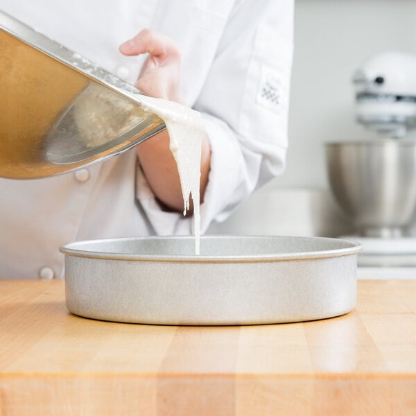 A person pouring dough into a Chicago Metallic round cake pan.