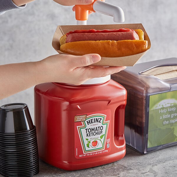 A person using a Heinz tomato ketchup pump to pour ketchup onto a hot dog.